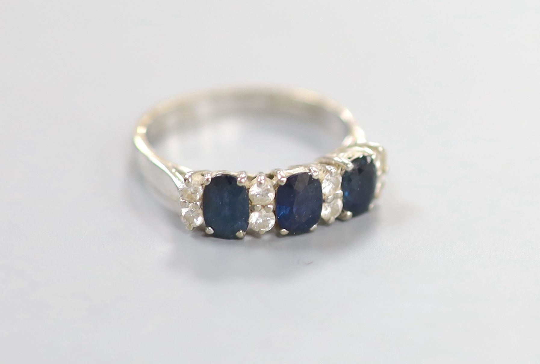 A modern 18ct white gold and three stone sapphire set half hoop ring with diamond set spacers, size N/O, gross 3.3 grams.